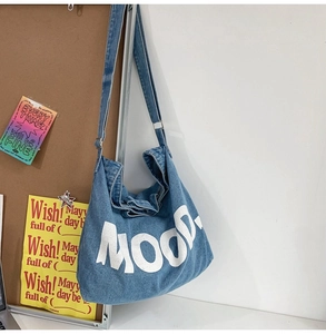 Detail view of a denim crossbody bag with white MOOD letter print and soft fabric texture