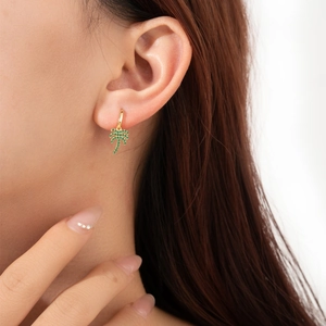 Golden palm tree drop earrings with green gemstones worn by model on white background
