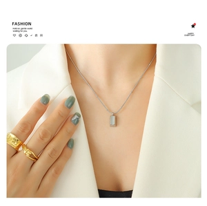 Gros plan d'un collier pendentif argenté rectangulaire porté avec des bagues dorées chics