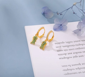 Macro shot of S925 silver dinosaur earrings with green pavé crystals on a white book