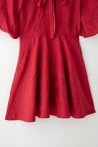 Gros plan de la robe rouge à manches bouffantes avec tissu gaufré et nœud au dos