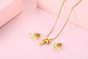 Detail of gold geometric V-shaped necklace and earring set on a pink display