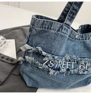 Gros plan du sac cabas en denim bleu avec bords effilochés et broderie blanche stylée