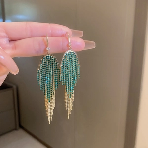 Detail of long gold tassel earrings with vibrant green rhinestones and elegant dangles