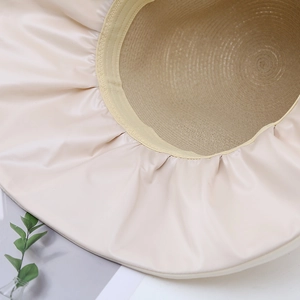 Détail du chapeau de soleil montrant le bord en tissu blanc cassé et la paille tressée