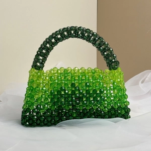 Detailed view of handmade gradient green acrylic beaded handbag on white textured fabric