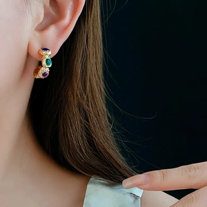 Close-up of vintage geometric gold C-shaped earrings with blue, green and purple gems
