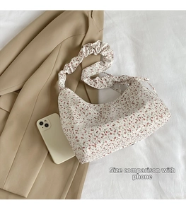 Floral underarm bag size reference with a smartphone on textured fabric background