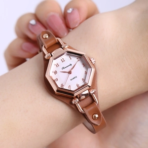 Détail d'une montre à quartz hexagonale or rose avec bracelet en cuir à rivets marron au poignet