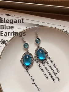 Detail of vintage filigree silver earrings with blue resin oval stones on white ceramic
