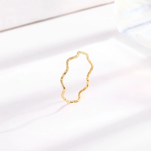Minimalist gold wavy textured titanium steel ring on a white surface with shadows