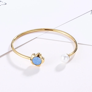 Detailed close-up of a gold open cuff bracelet with blue flower crystal and white pearl