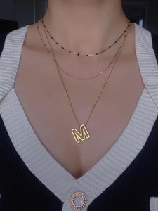 Detailed view of triple-layered gold necklaces with M pendant on a model's neck