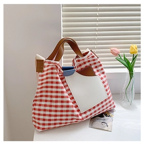 Detail view of red plaid canvas tote bag with brown handles and a white front pocket