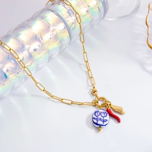 Detail of gold necklace featuring chili, ceramic floral disk, and shell charms on a prism base