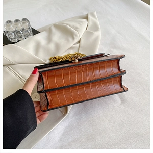 Detail view of brown crocodile texture chain bag with accordion side design and gold hardware