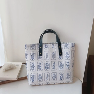 Close-up of canvas tote bag with blue botanical print and green leather handle with rivets