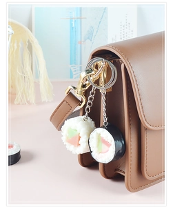 Dettaglio di portachiavi a forma di sushi e onigiri appesi a una borsa di pelle