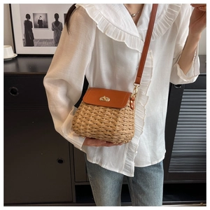 Detail of handmade straw crossbody bag with brown leather trim and golden metal lock