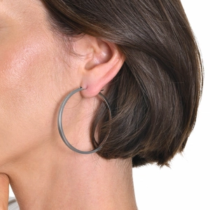 Macro side view of a large polished silver hoop earring worn by a model for size