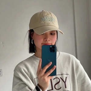 Detail of beige cotton baseball cap with blue Friends embroidery worn by a model