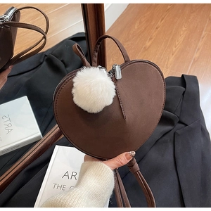 Detail einer dunkelbraunen herzförmigen Tasche mit Plüsch-Anhänger und Reißverschluss