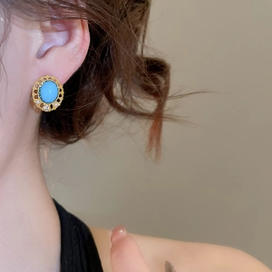 Detail of vintage gold earrings with turquoise gemstone and white bead accents on ear