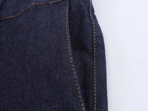 Dettaglio macro delle cuciture gialle e della trama del denim sui jeans blu scuro
