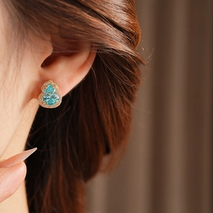 Detail of gold gourd stud earring with a blue gemstone and pavé diamonds on a model