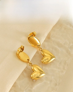Detailed shot of gold-plated heart earrings with LOVE engraving on silk background