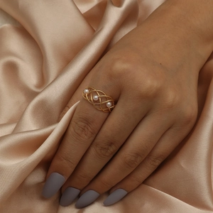 Fashionable cross-woven hollow gold ring with three elegant pearls on a silk background