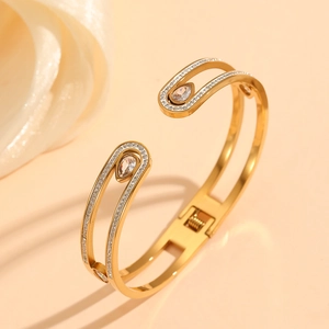 Détail d'un bracelet doré orné d'un zircon poire et de pierres pavées sur fond chaleureux