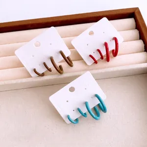 Three sets of colorful C-shaped enamel earrings in brown, red, and blue on cards