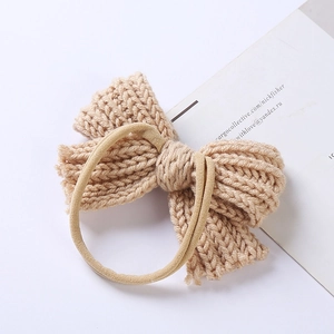 Close-up of beige knitted bow headband for babies with soft ribbed texture on white background