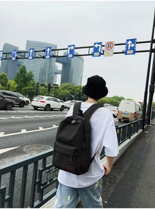Street style view of a black canvas backpack featuring brown leather zipper pulls