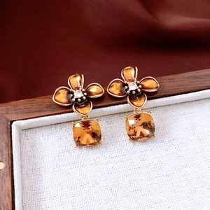 Macro view of gold-plated flower earrings with amber crystals on a wooden tray