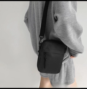 Detail of minimalist black nylon crossbody bag with zipper pockets and webbing strap