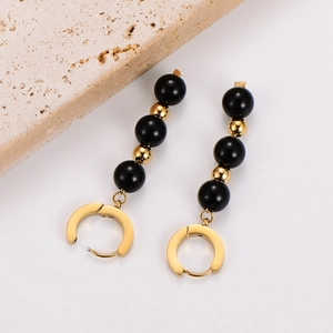 Detail of beaded long drop earrings with black and gold beads on stone texture