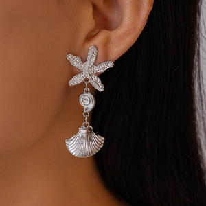 Macro shot of silver shell and starfish asymmetric earrings with metallic textures
