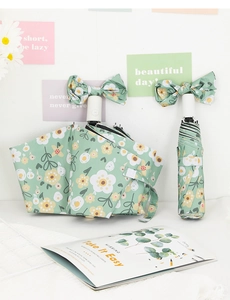Detail of mint green folding umbrella with floral pattern and bow on the handle