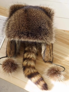 Detailed view of raccoon fur style winter hat with striped tail and pompom accents