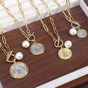 Detailed shot of golden paperclip necklaces with St. Benedict medal and pearl pendants