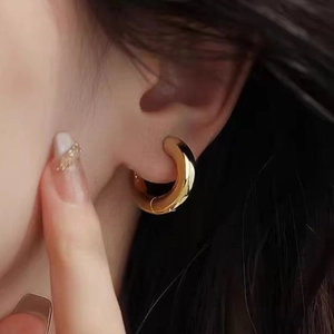 Close-up of chunky gold hoop earrings with a high-polished finish on a female model