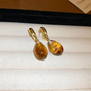 Detail of gold C-shaped earrings with amber resin waterdrop pendants on a beige tray