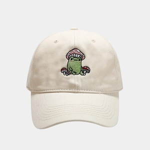 Close-up of cute cartoon frog and mushroom embroidery on beige cotton baseball cap