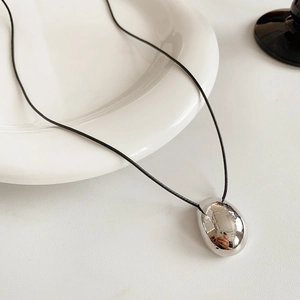 Détail d'un pendentif galet argenté sur cordon noir sur de la vaisselle en céramique