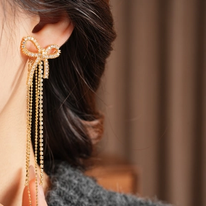 Close-up of elegant 18k gold plated bow earrings with dangling zircon tassels on model