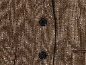 Macro detail of brown herringbone wool fabric with black matte buttons on a blazer