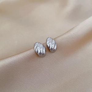Minimalist silver ribbed egg-shaped titanium steel stud earrings on champagne silk fabric