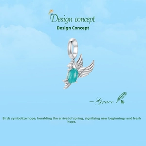 Detail of silver flying bird charm with green gemstone inlay against a blue sky
